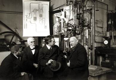 Paul Ehrenfest, Hendrik Lorentz, Niels Bohr, Heike Kamerlingh Onnes (1919)  in the cryogenic lab of Leyden, in front of the helium liquefier; Museum Boerhaave, Leiden 